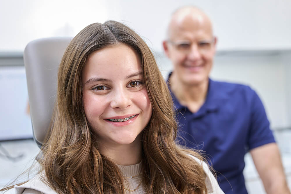 Frank Pflumm Kieferorthopädie Zahnarzt Dr. Pflumm mit einem lächelnden Mädchen, das eine Zahnspange trägt