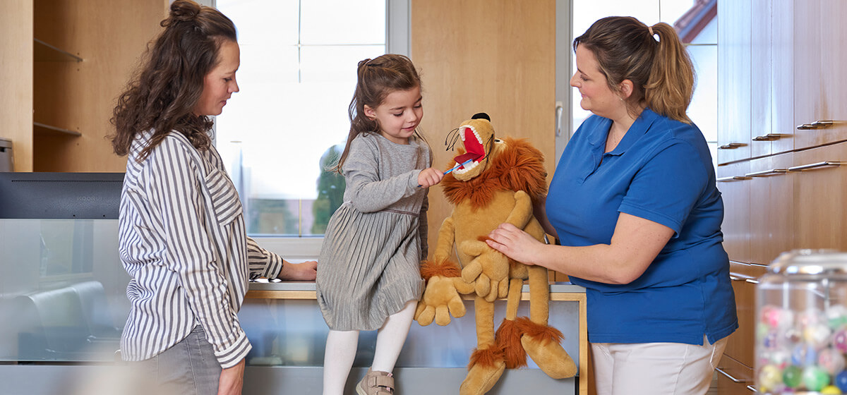 Zahnmedizinische Prophylaxe-Assistentin erklärt Kind und Mutter das richtige Zähneputzen 
