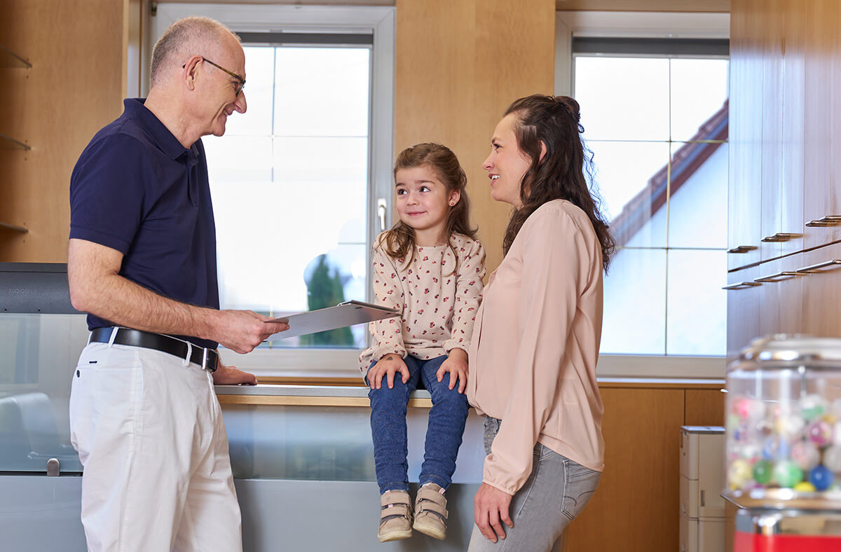 Kinderzahnarzt Dr. Frank mit Kind und Mutter im Beratungsgespräch am Empfang