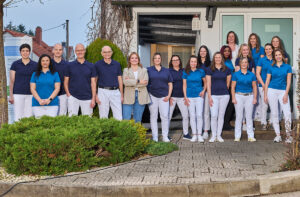 Gruppenbild der Zahnärzte mit ihrem gesamten Team vor der Zahnarztpraxis
