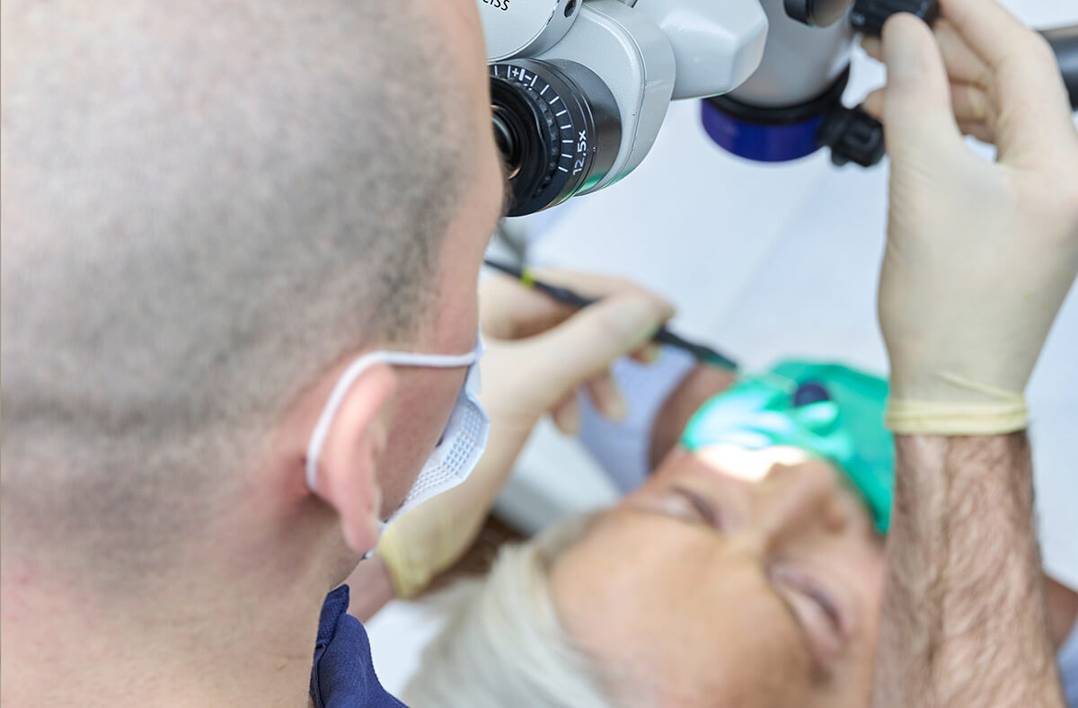 Zahnarzt Kramer bei der Wurzelkanalbehandlung mit Mikroskop über eine Patientin gebeugt