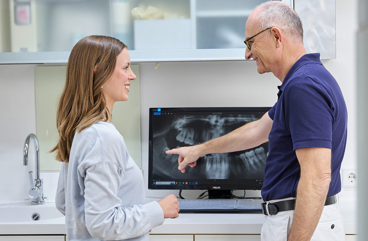 Zahnarzt Dr. Frank mit Patientin vor dem Bildschirm mit Röntgenbild vor chirurgischen Eingriff Zahnarzt Dr. Frank mit Patientin vor dem Bildschirm mit Röntgenbild vor chirurgischen Eingriff