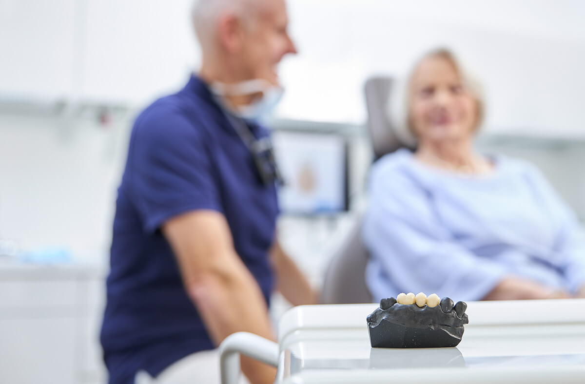 Dr. Pflumm mit Patientin im Hintergrund, im Vordergrund Modell für Zahnersatz